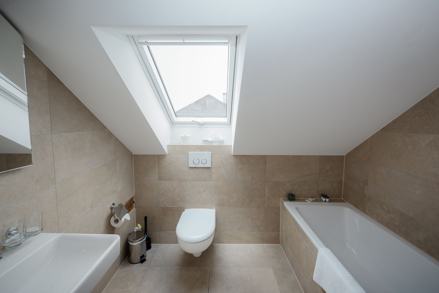 A modern bathroom with a skylight, a toilet, a bathtub, and a sink.