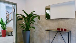 A modern lobby with a potted plant, a chair, a console table with red glasses, and a mirror on the wall. - Zurich Furnished Homes (Zürich)