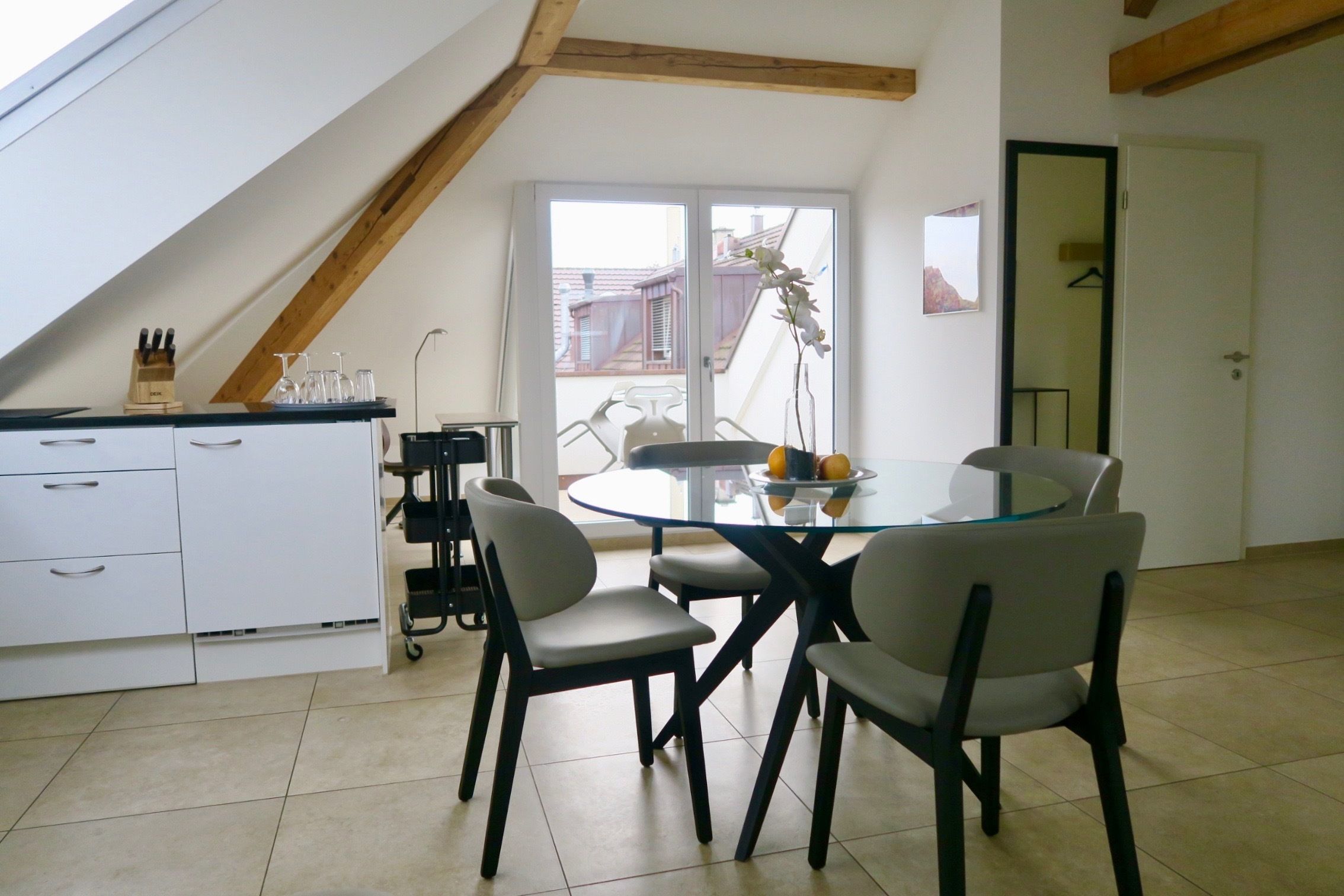 A dining area with a glass table and chairs, a kitchen with white cabinets, and a view through a sliding door.
