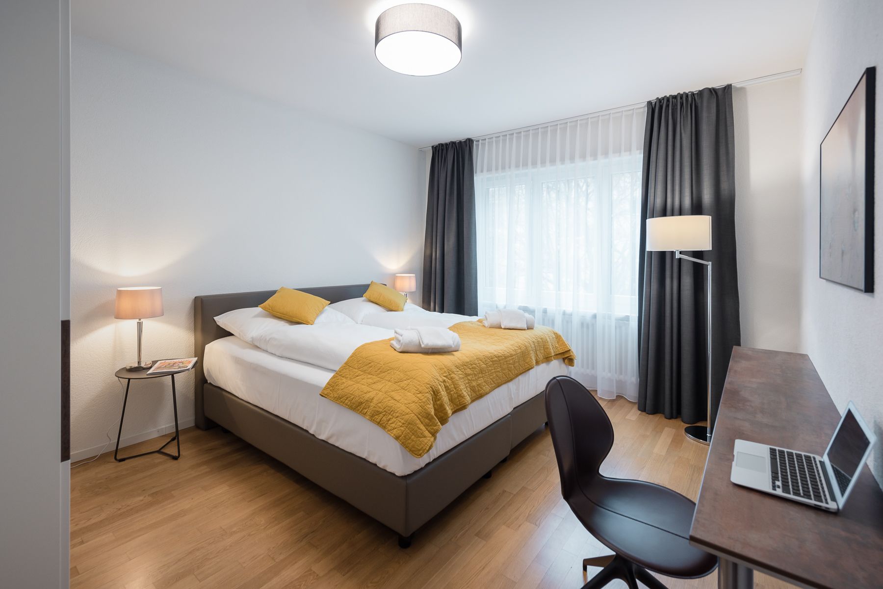 Ein modernes Hotelzimmer mit einem Bett, einem Schreibtisch, einem Stuhl und einem Laptop.