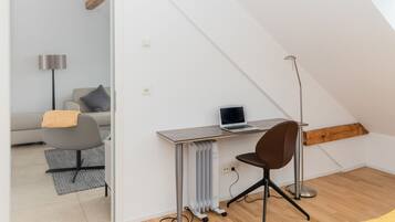Een moderne loft slaapkamer met een schuine plafond, een ingebouwd bureau met een laptop, een bruine bureaustoel, en een radiator.