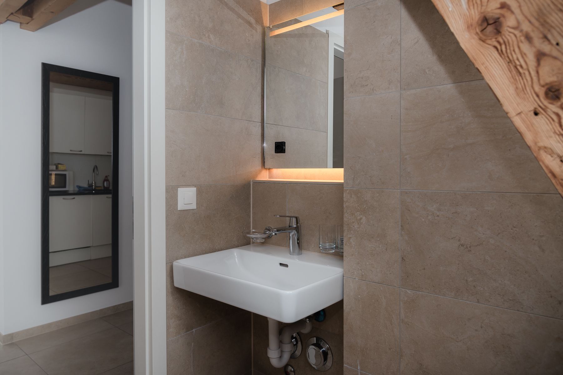 A modern bathroom with a white sink, a mirror, and beige tiles.