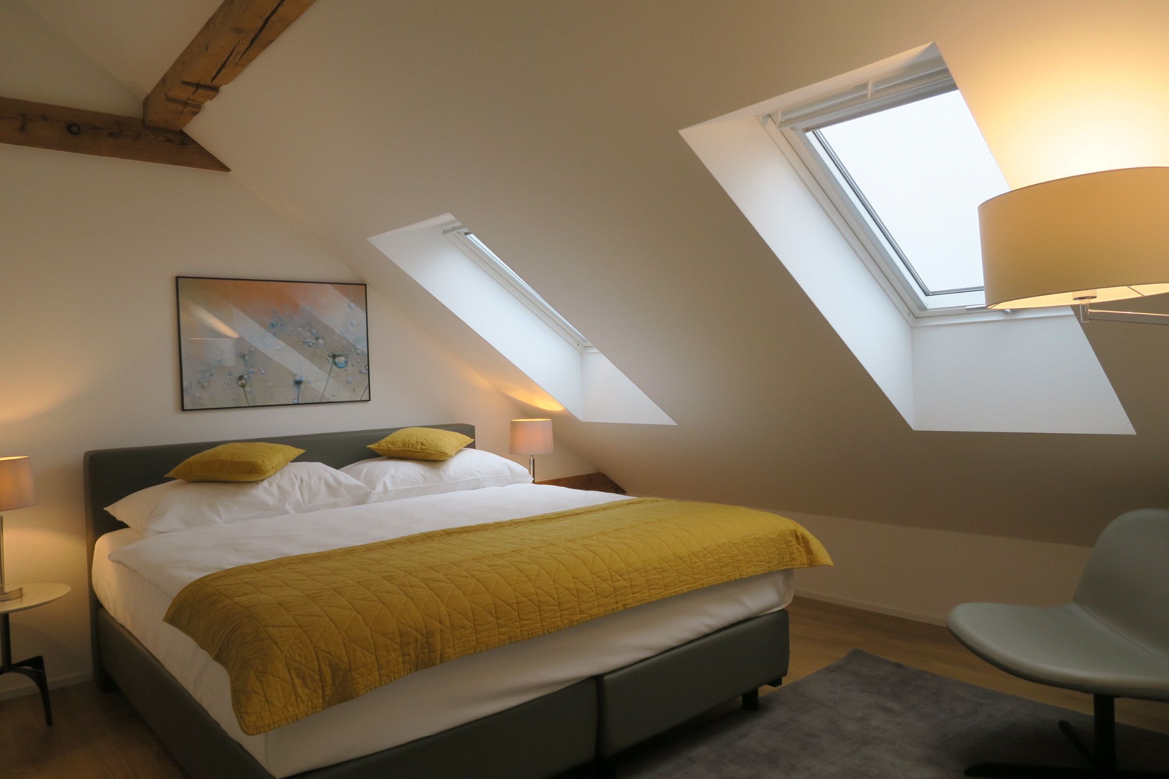 A bedroom with a bed, a chair, a painting, and skylights.