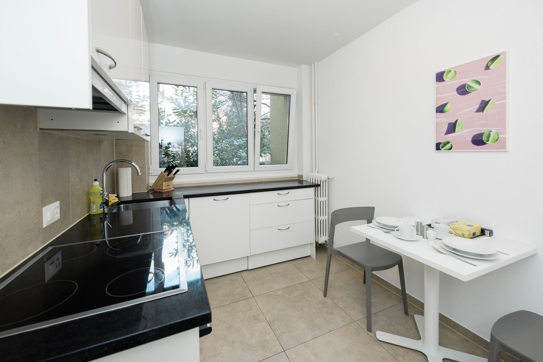 A modern kitchen with white cabinets, a black countertop, a window, and a dining area with a table and chairs.