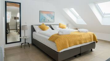 A modern bedroom with a large bed, a bedside table, a floor lamp, a painting, and skylights.
