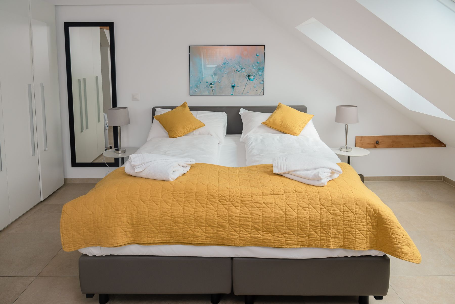A modern bedroom with a bed, two bedside tables, a mirror, and a painting on the wall.