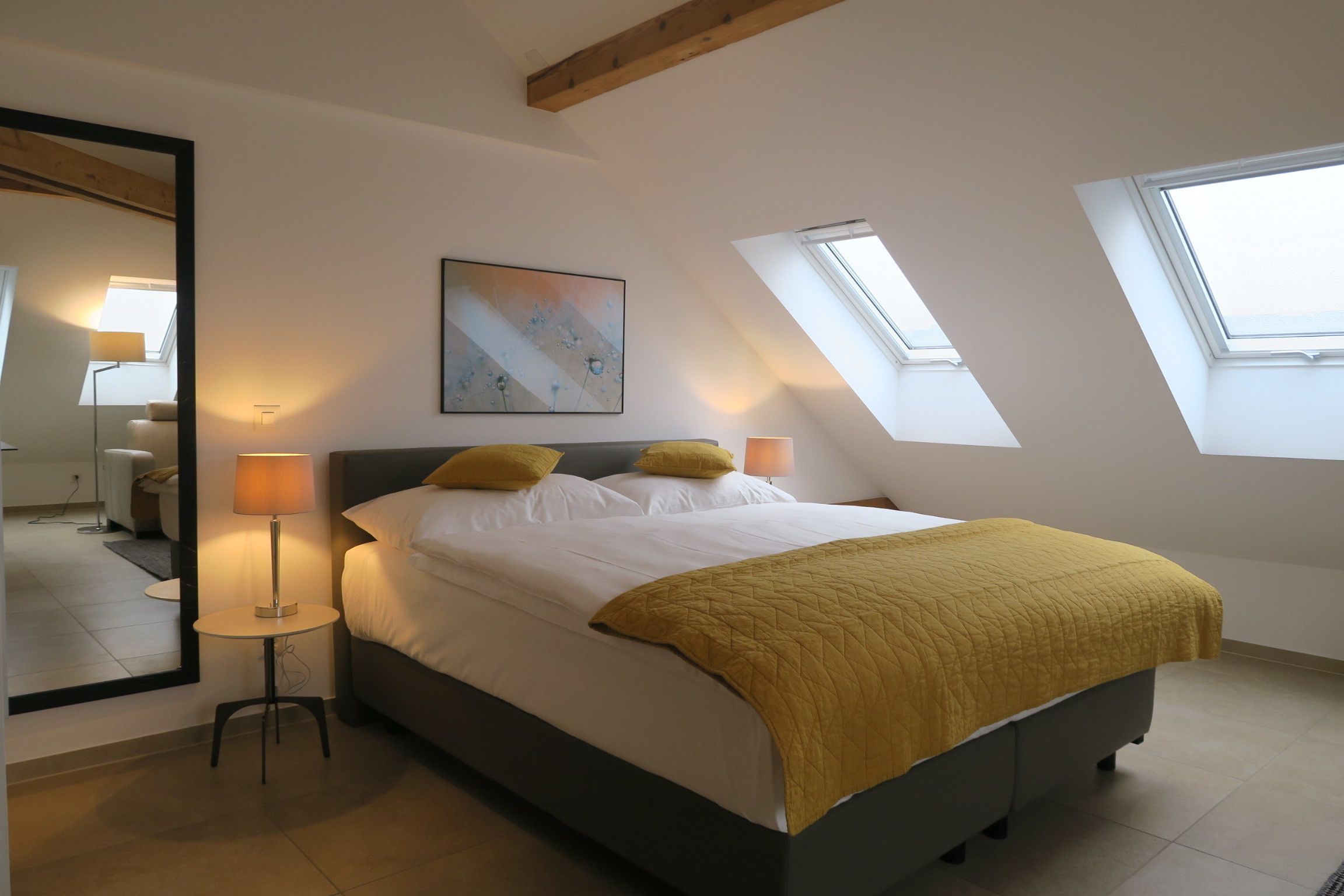 Un dormitorio con cama, dos lámparas de noche, un cuadro y tragaluces.