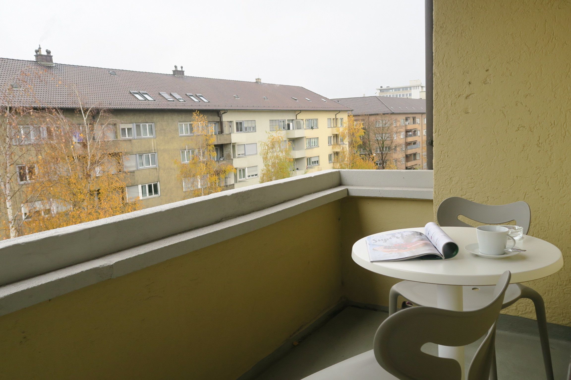 Ein Balkon mit Tisch und Stühlen, der auf eine Reihe von Wohngebäuden blickt.