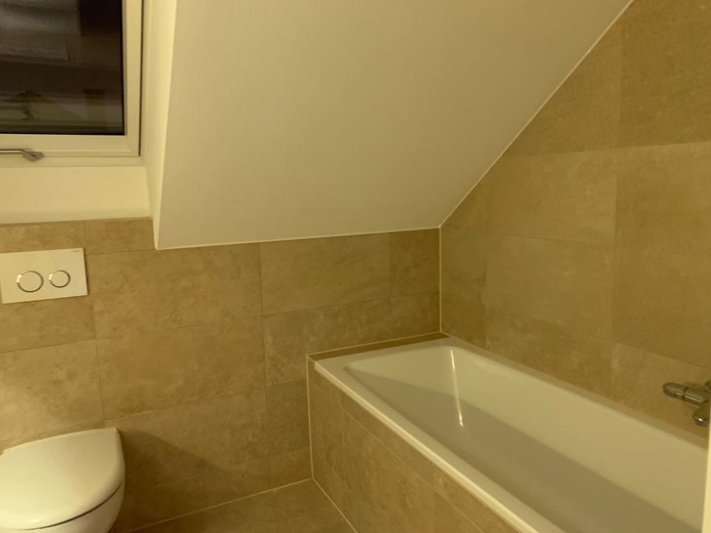 Un baño con bañera, inodoro y azulejos color beige.
