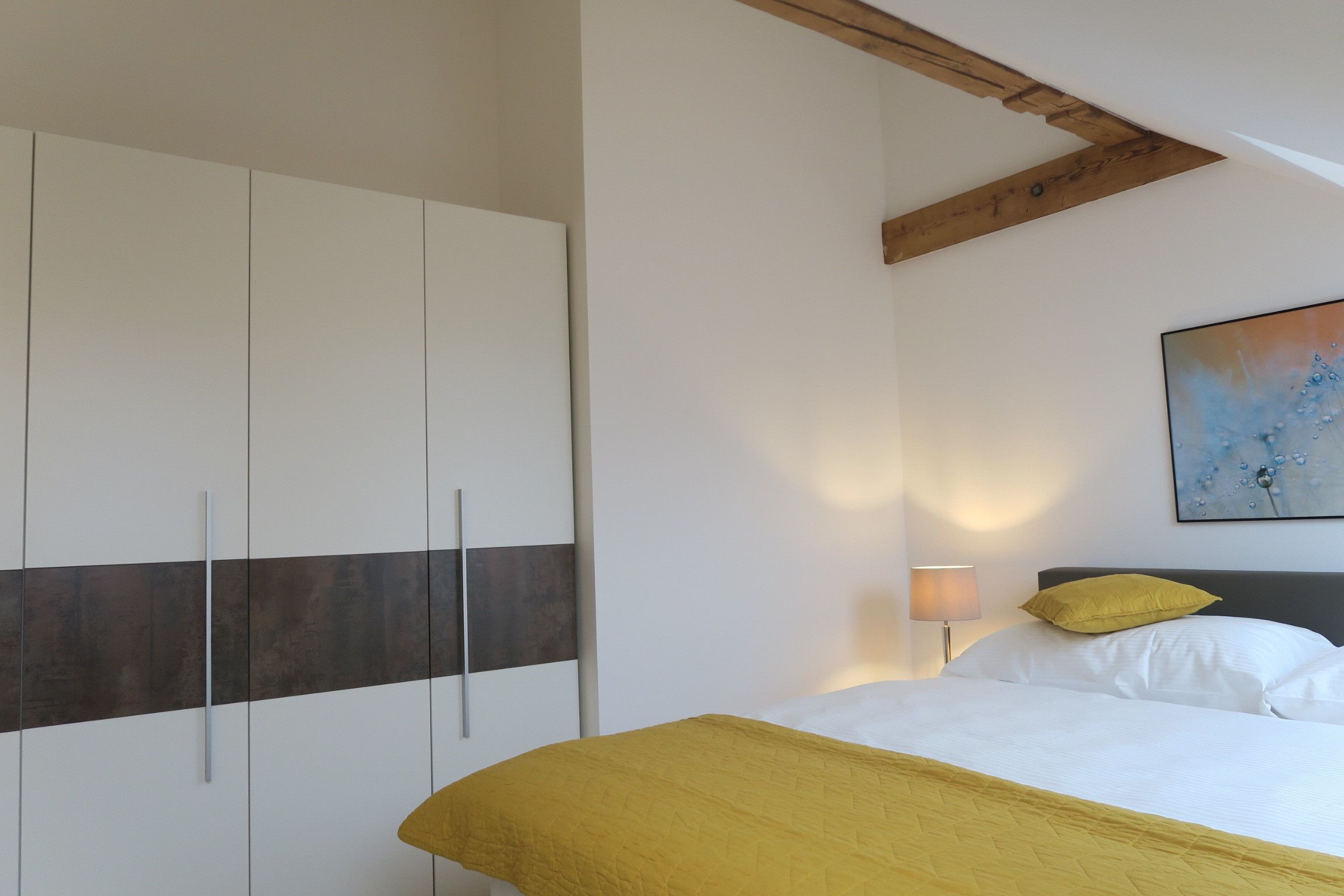 A bedroom with a bed, a wardrobe, a painting on the wall, and a lamp.