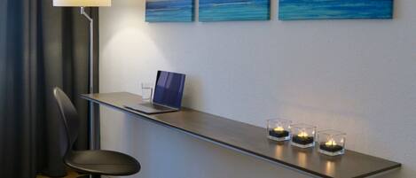 A modern room with a desk, a laptop, and three paintings of the ocean.