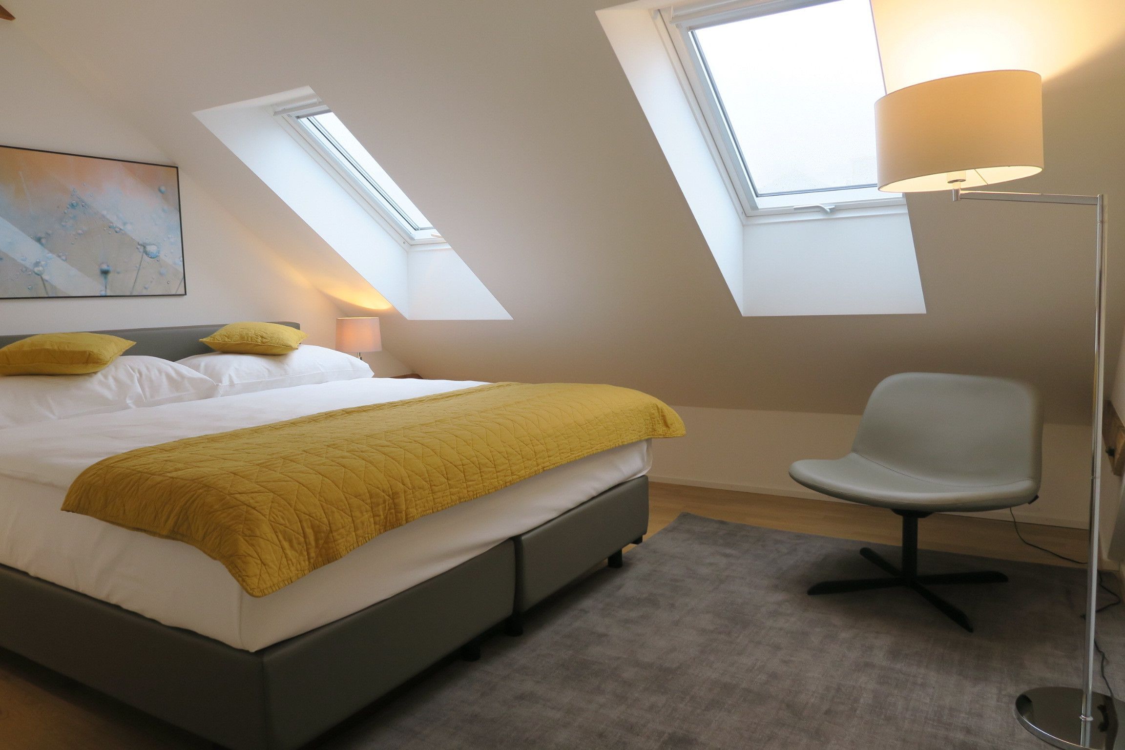 A bedroom with a bed, a chair, a floor lamp, and skylights.
