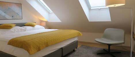 A bedroom with a bed, a chair, a floor lamp, and skylights.