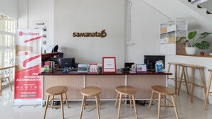 A reception area with a desk, computer, and chairs. There is a sign for RedDoorz and a wall-mounted sign with the text "samanataB". - Lantai Dua Jogja - Hostel (Depok)