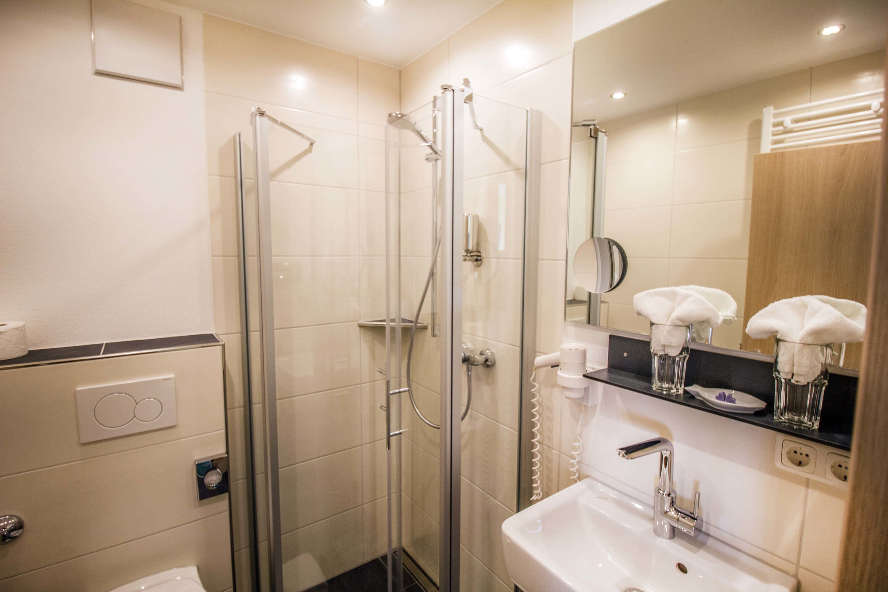 A modern bathroom with a glass-enclosed shower, a sink with a mirror, and a towel rack with towels.