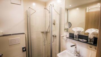 A modern bathroom with a glass-enclosed shower, a sink with a mirror, and a towel rack with towels.