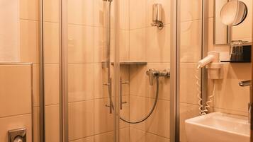 A glass-enclosed shower stall with a white towel on the floor, a sink with a mirror, and a toilet.
