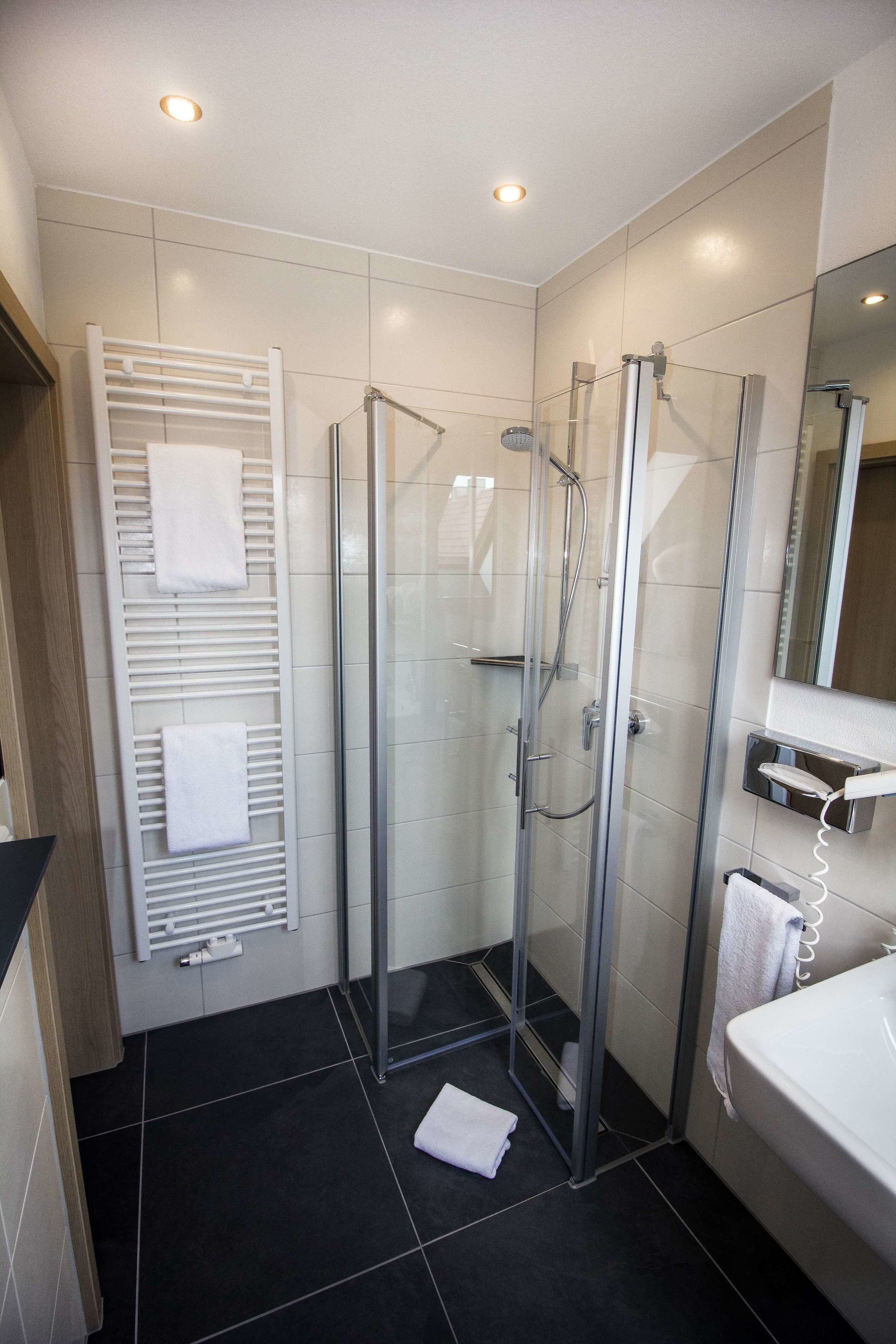 Un bany modern amb un plat de dutxa de vidre, un suport per tovallons blanc i un mirall sobre el lavabo.