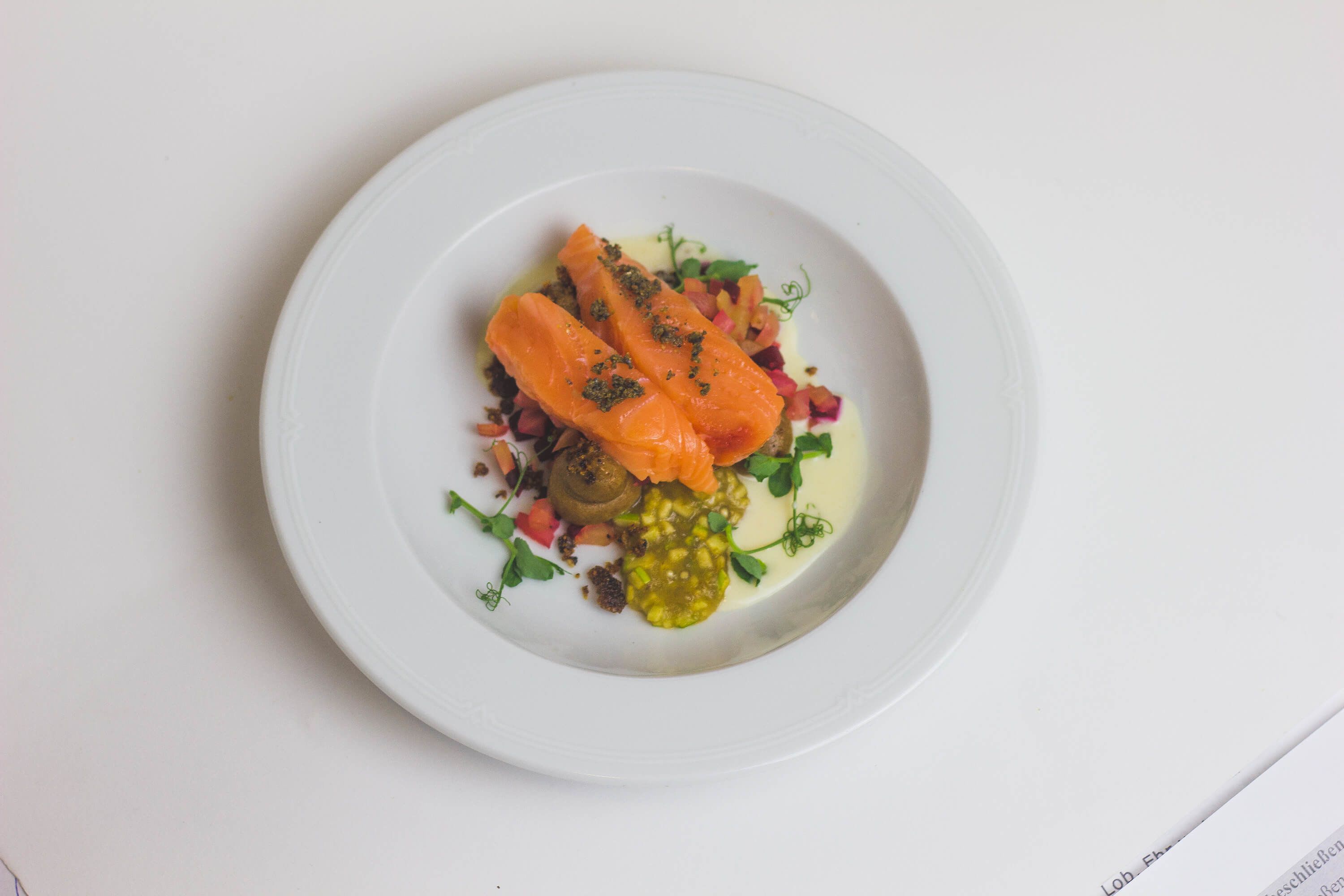 A white plate with salmon, mushrooms, and greens.
