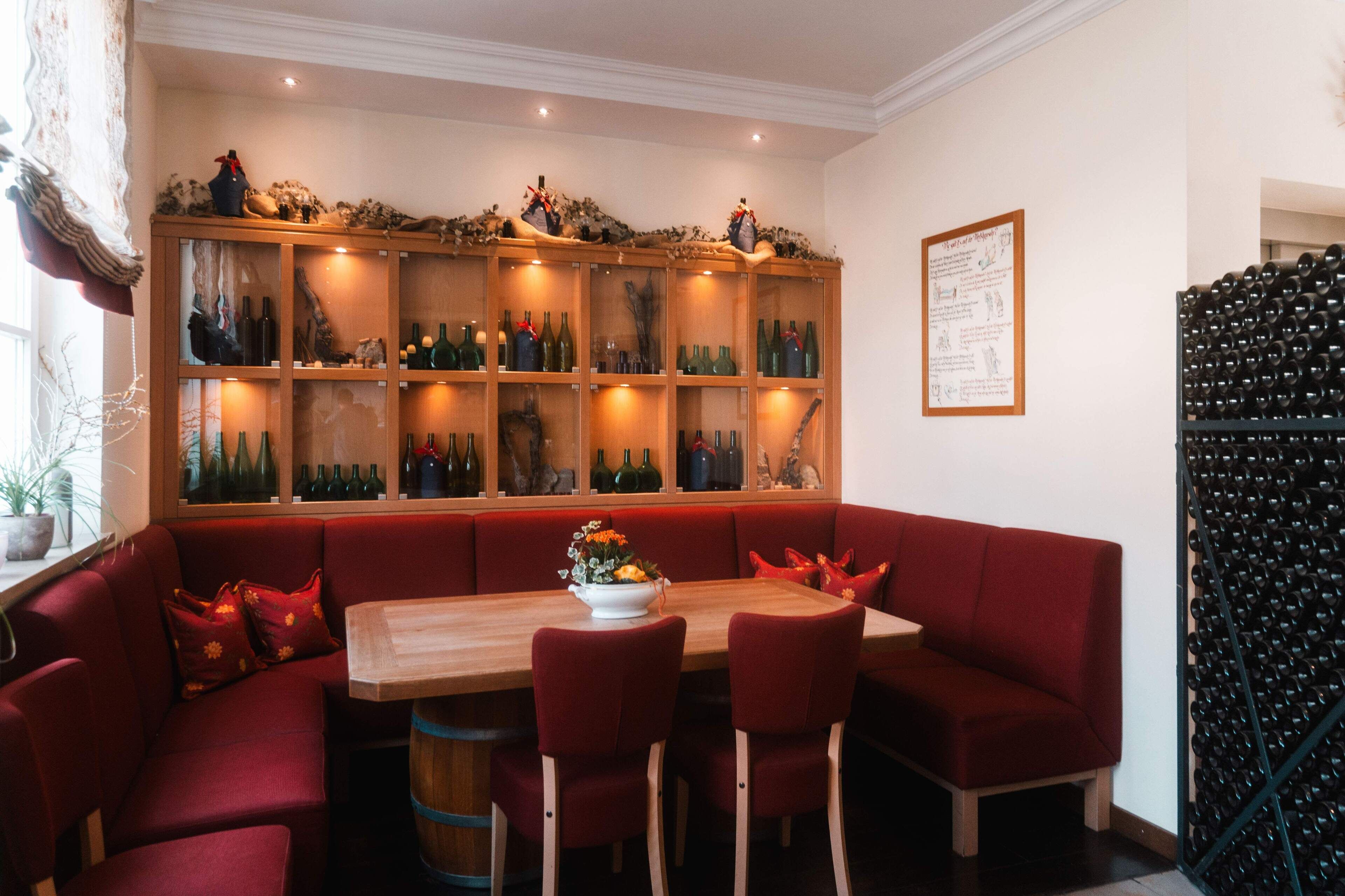A dining area with a wooden table, red upholstered seating, and a wine display cabinet.