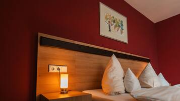 Quarto de hotel com cabeceira de madeira, mesa de cabeceira com abajur e cama com almofadas brancas.