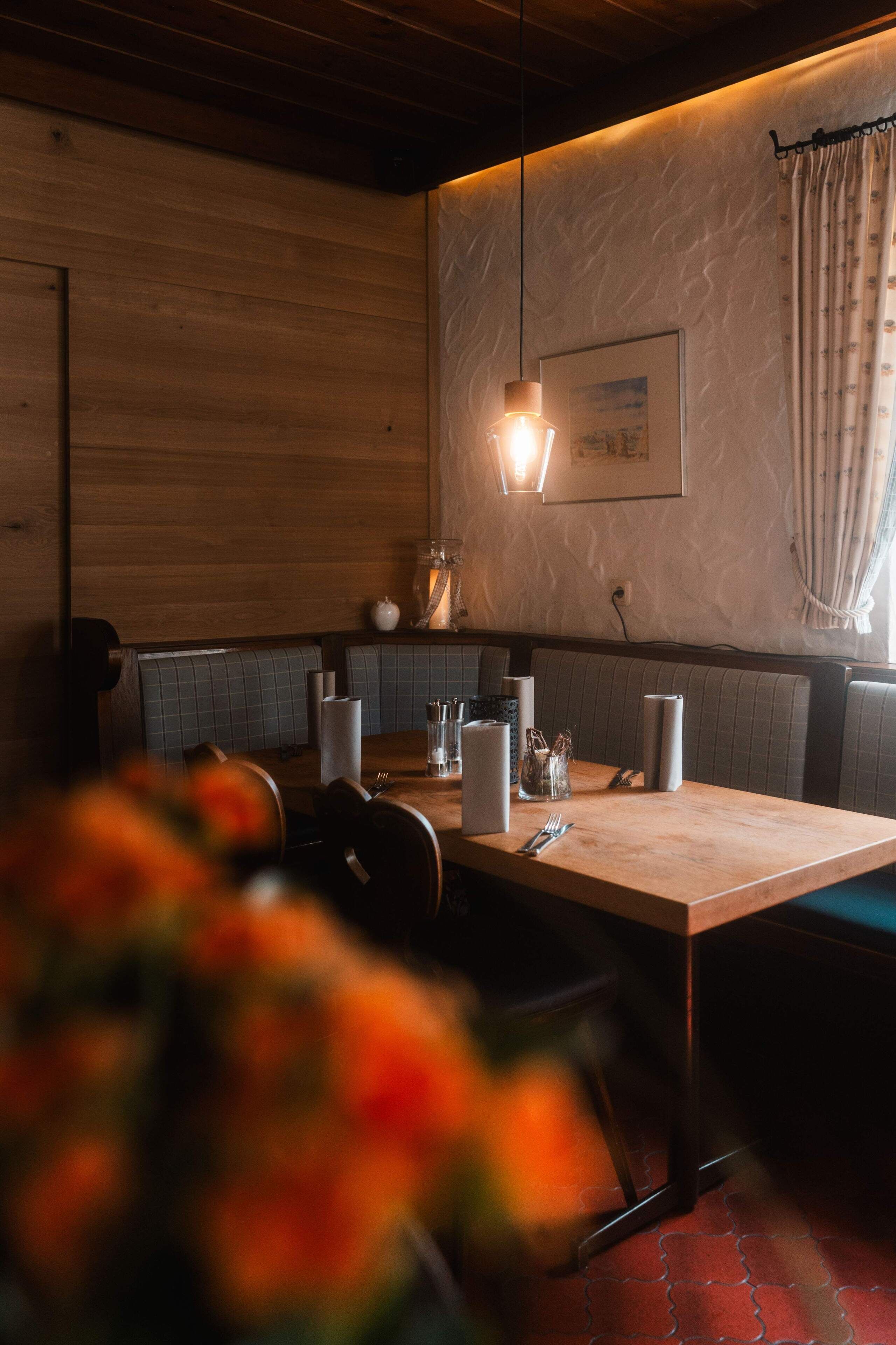 Un restaurant aux murs en bois, une table dressée avec des assiettes, des verres et des couverts, et un luminaire suspendu.