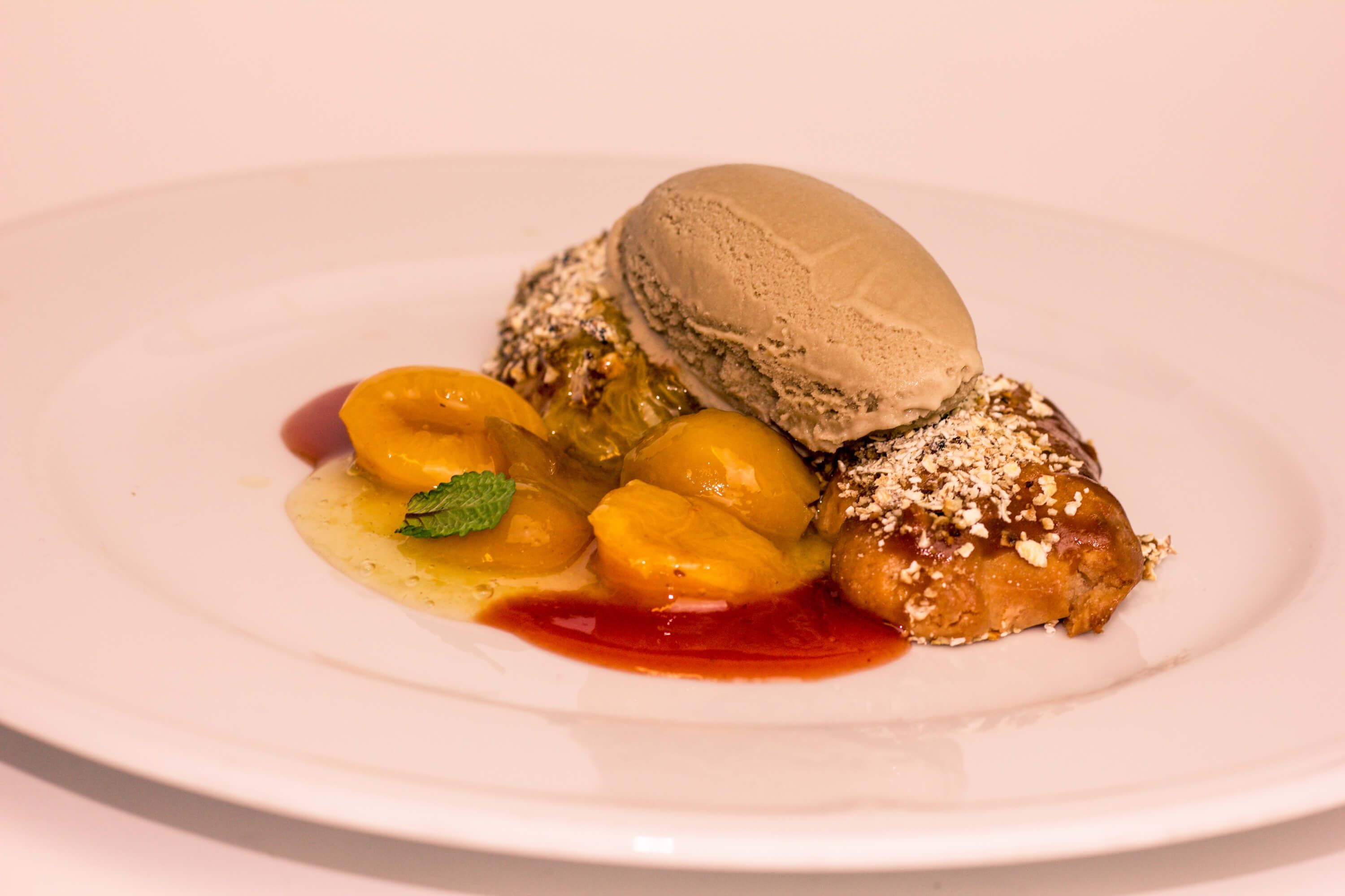 A dessert plate with a scoop of ice cream, peaches, and a mint leaf.