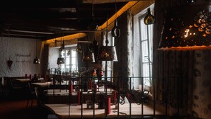 A dimly lit restaurant with wooden tables and chairs, hanging light fixtures, and a view of the street outside.