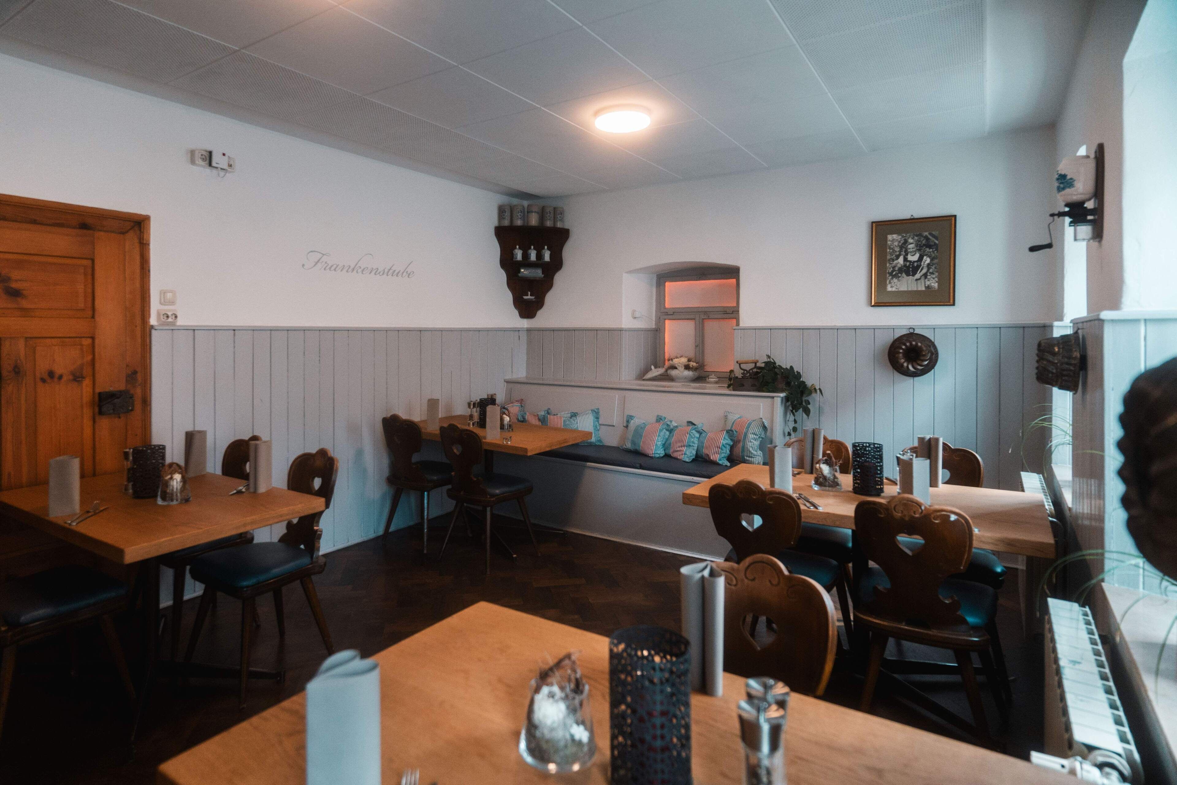 Un restaurante con mesas y sillas de madera, un piano y una pared con un cuadro enmarcado y una estantería con botellas.