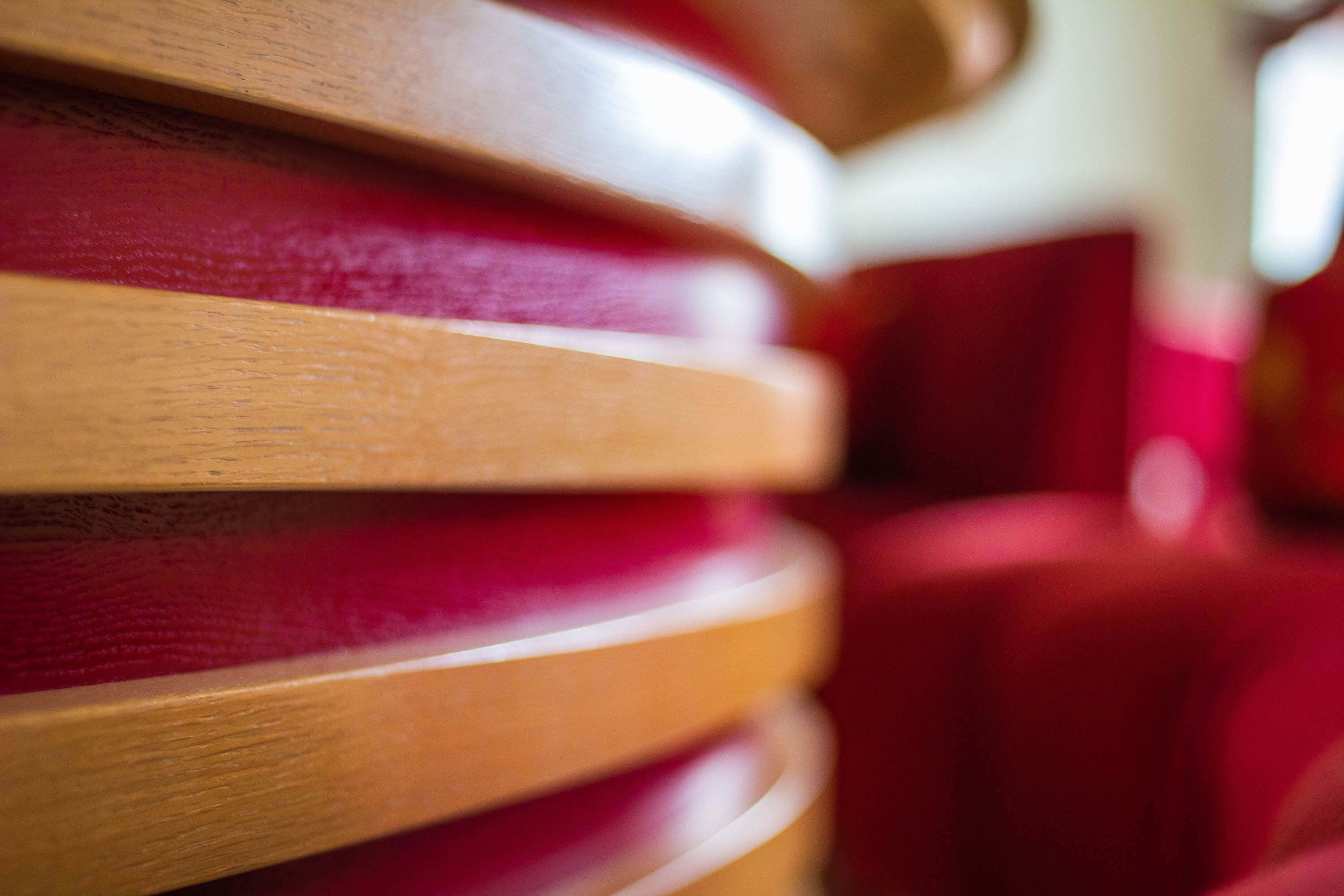 Primer plano de listones de madera apilados con un asiento tapizado de rojo al fondo.