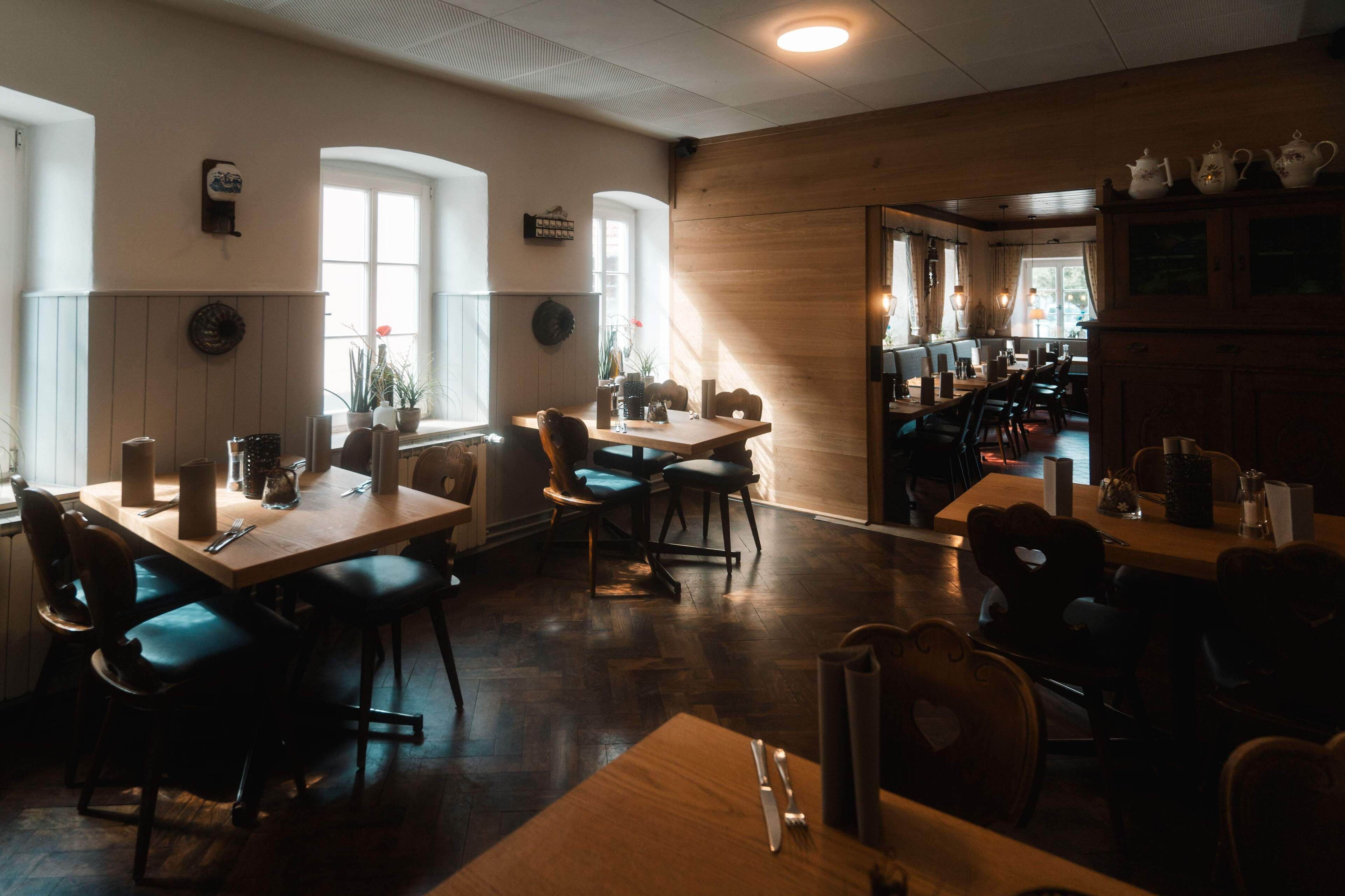 A cozy restaurant with wooden tables and chairs, large windows, and a warm ambiance.