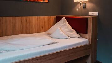 Una cama individual con cabecera de madera, ropa de cama blanca y alfombra roja.