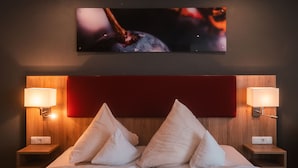 Ein Hotelzimmer mit einem großen Bett, zwei Nachttischen mit Lampen, einem roten Kopfteil und einem an der Wand befestigten Fernseher.
