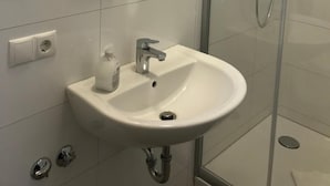 Un baño moderno con un espejo redondo, un lavabo y una ducha con cerramiento de vidrio.
