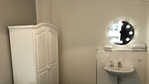 Habitación de hotel con cama, armario, baño con lavabo y espejo, y un perchero.