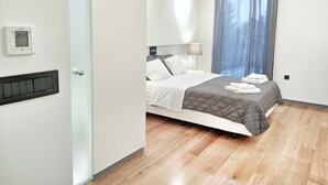Une chambre d’hôtel moderne équipée d’un lit, d’un thermostat, d’une fenêtre avec des rideaux et d’un plancher en bois.