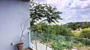 Un balcon avec une plante en pot, une chaise rouge et une vue sur une voiture rouge garée dans la rue.