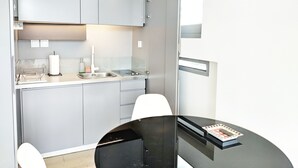 Une cuisine moderne avec des meubles gris, un plan de travail noir et une porte en verre donnant sur un coin repas avec une table noire et des chaises blanches.