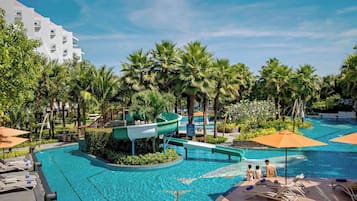 Relax by the pool surrounded by palm trees and lounge chairs, with a water slide and adjacent building with balconies.