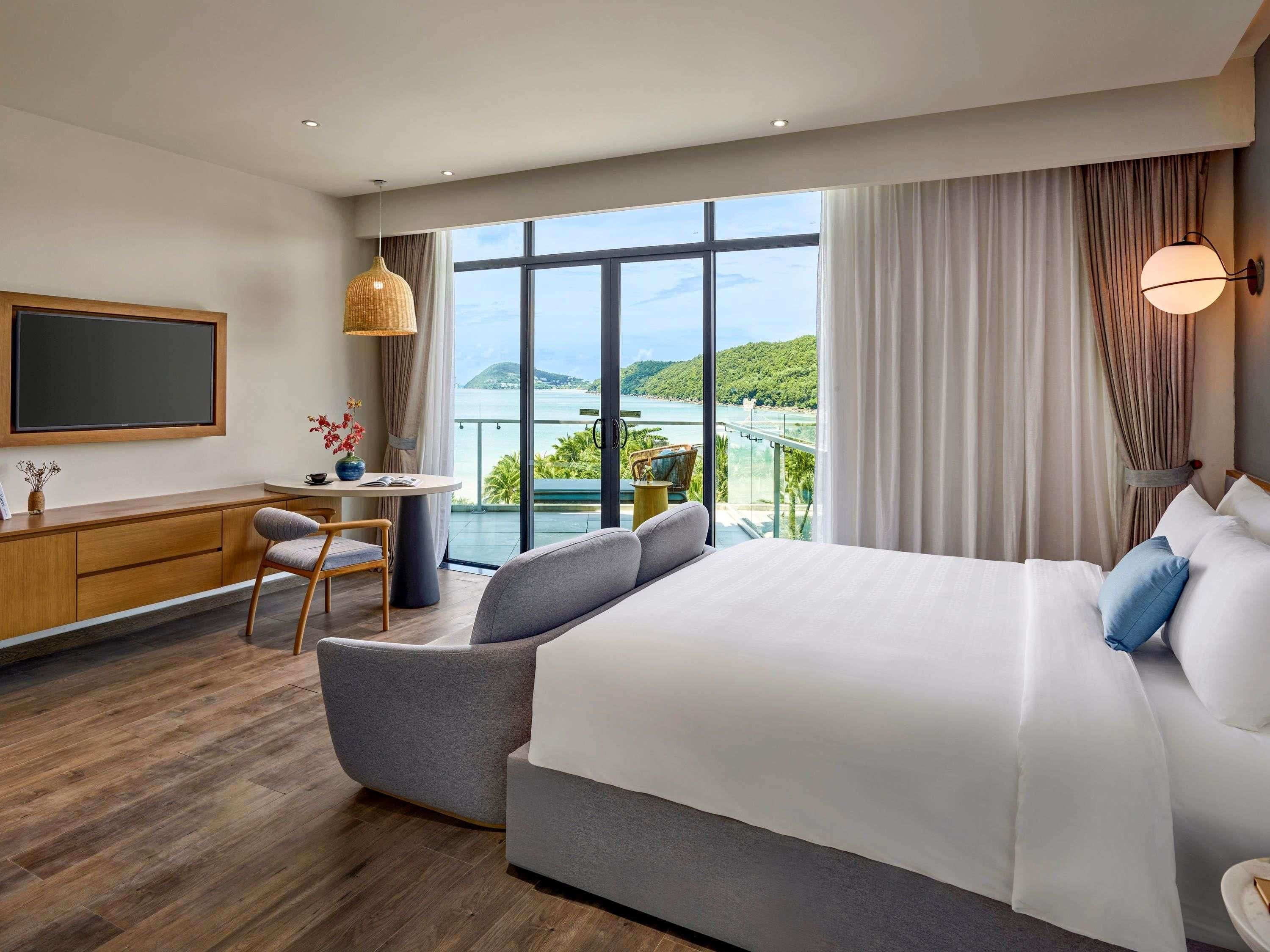 A hotel room with a large bed, a desk, a chair, and a view of a body of water.