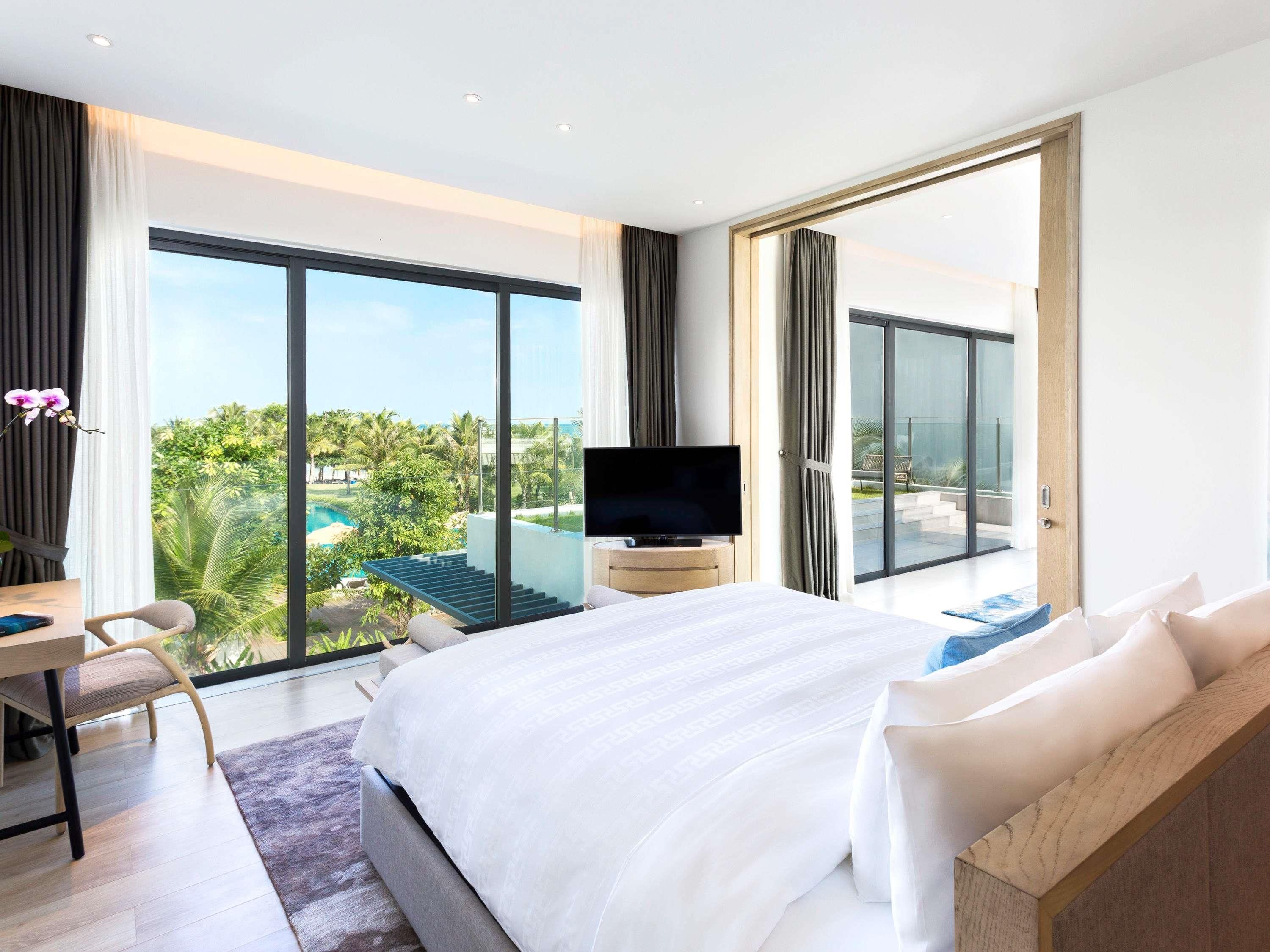 A modern hotel room with a large bed, a TV, a desk, and a balcony with a pool view.
