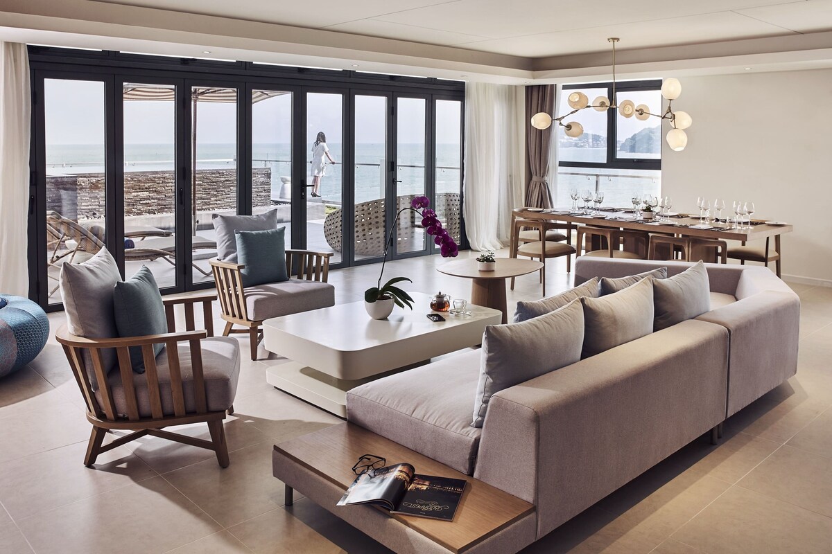 Una sala de estar moderna con un sofá grande, una mesa de centro y un comedor con vistas al mar.
