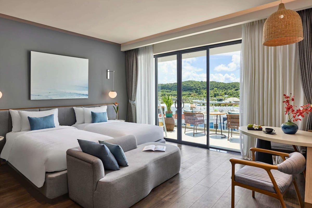 Habitación de hotel moderna con una cama grande, un sofá, una mesa de comedor y vistas al paisaje.