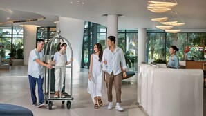 Un moderno hall de hotel con mostrador de recepción, un carrito de equipaje y grandes ventanales con vistas a zonas verdes.
