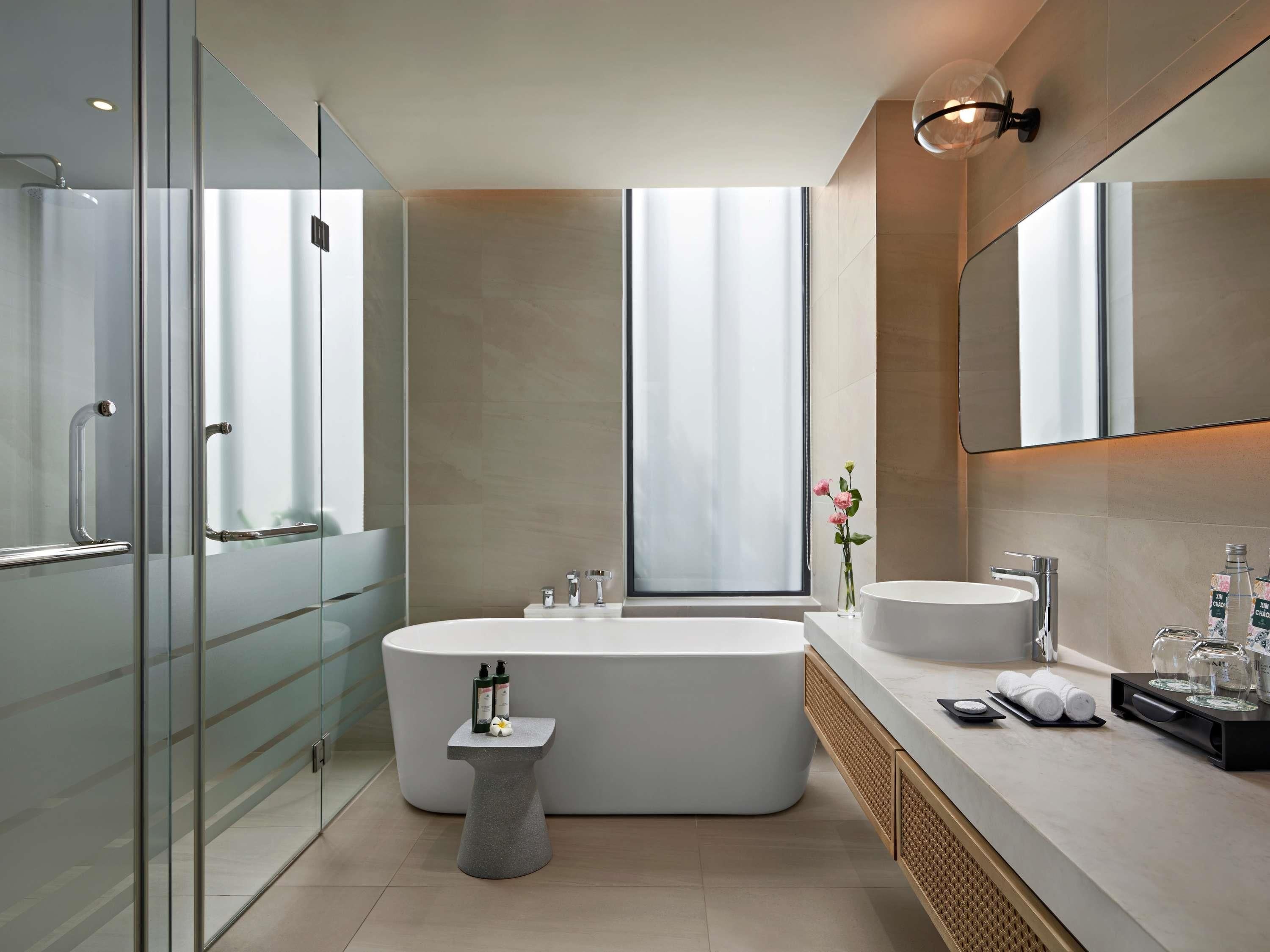 A modern bathroom with a glass shower enclosure, a freestanding bathtub, a vanity with a sink, and a large mirror.
