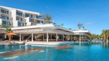 Et moderne hotel med en stor swimmingpool, udendørs siddepladser og palmer.