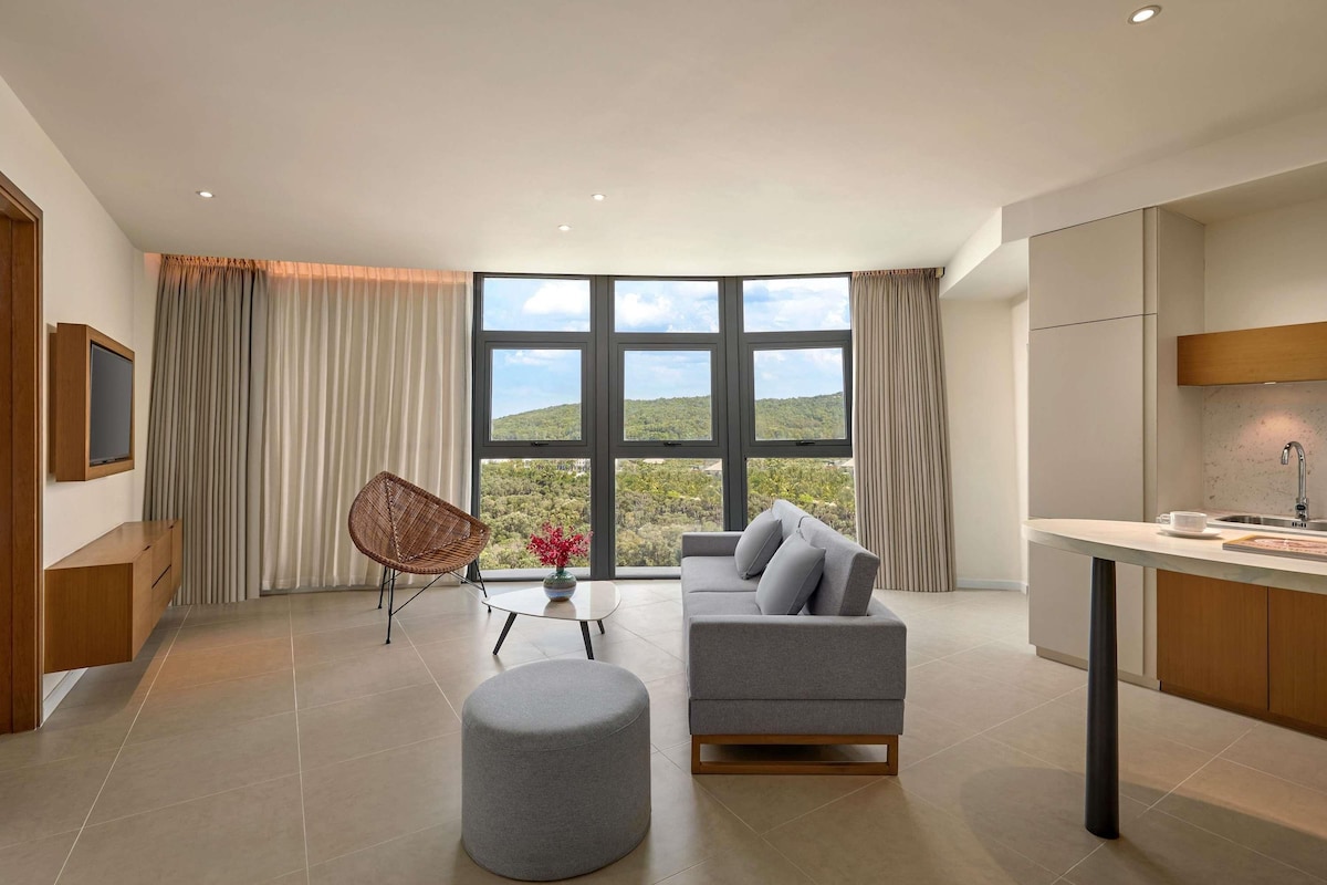 Un espacio de estar moderno con un sofá, reposapiés y una zona de comedor con mesa y sillas.