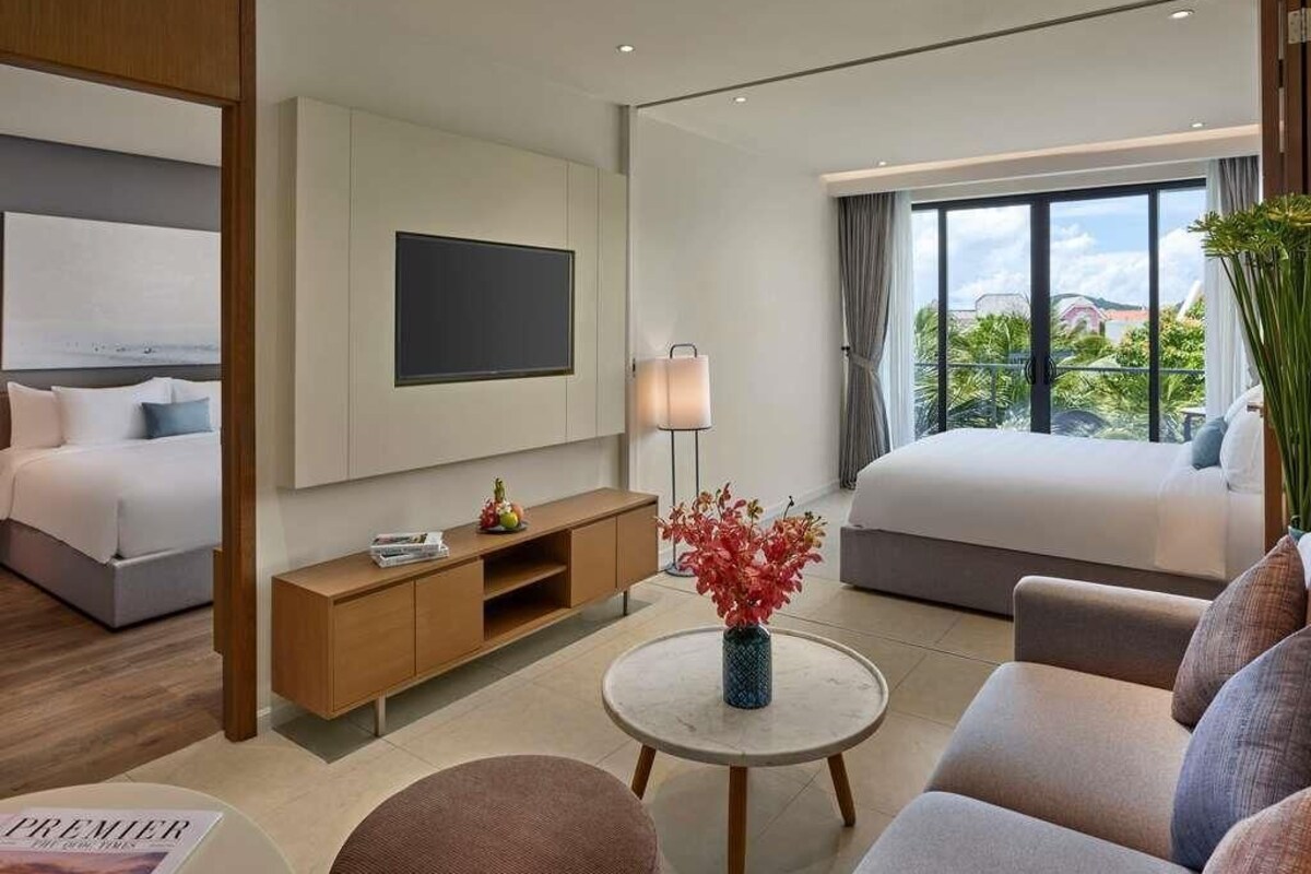 Una habitación de hotel moderna con cama, sofá, televisión, mesita de noche y ventana con vistas.