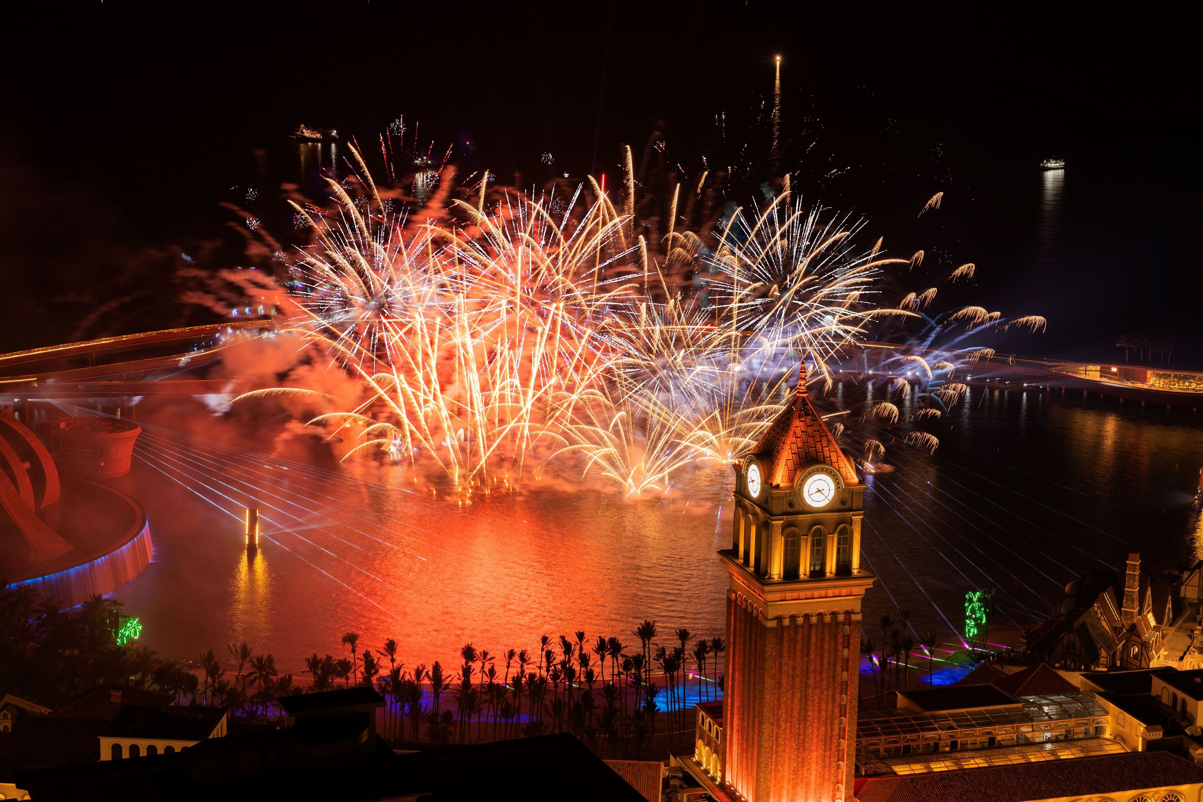 A clock tower with a water body in the background, illuminated by fireworks.
