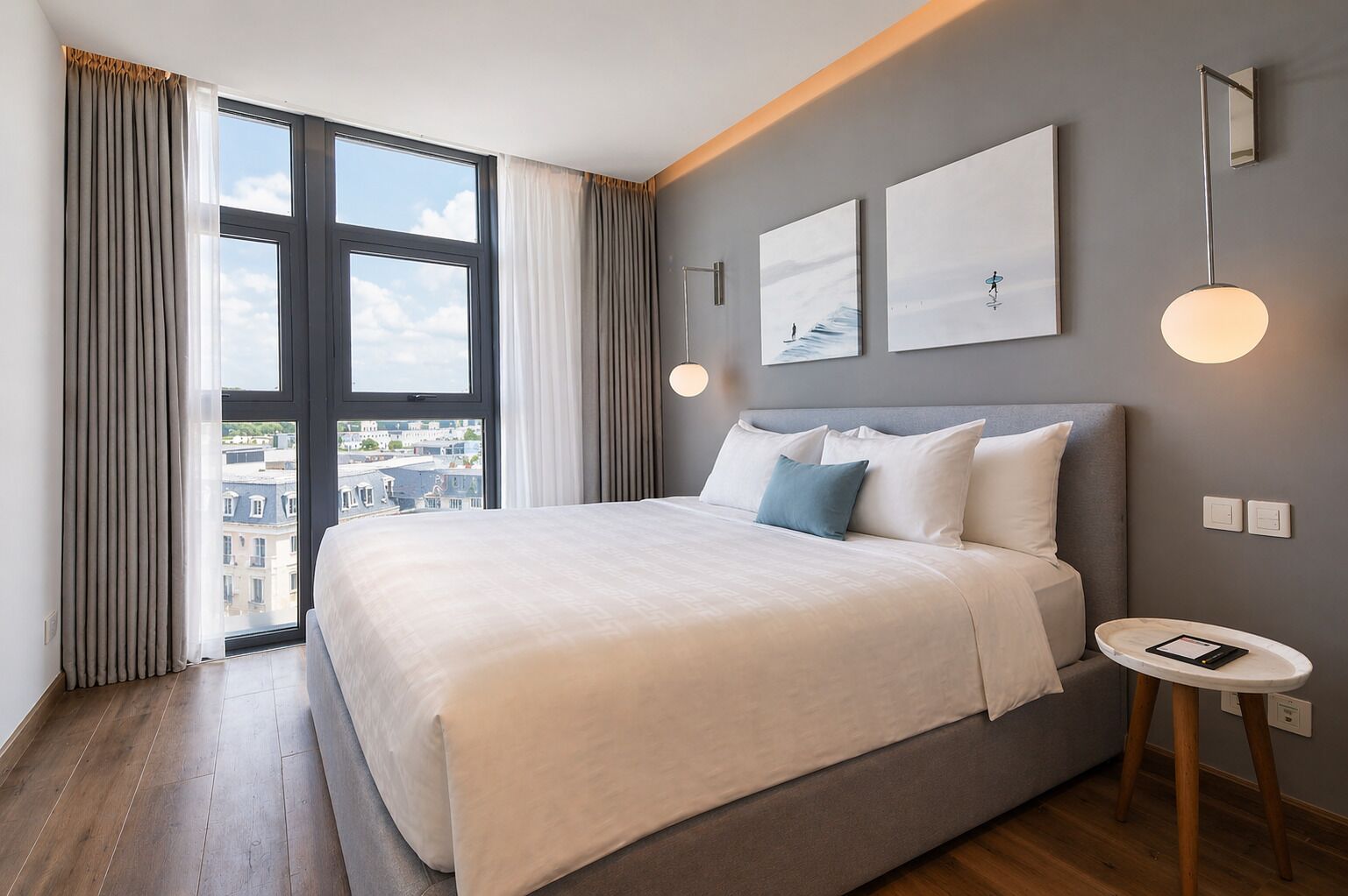 A modern hotel room with a large bed, a small bedside table, and a view of the city through large windows.